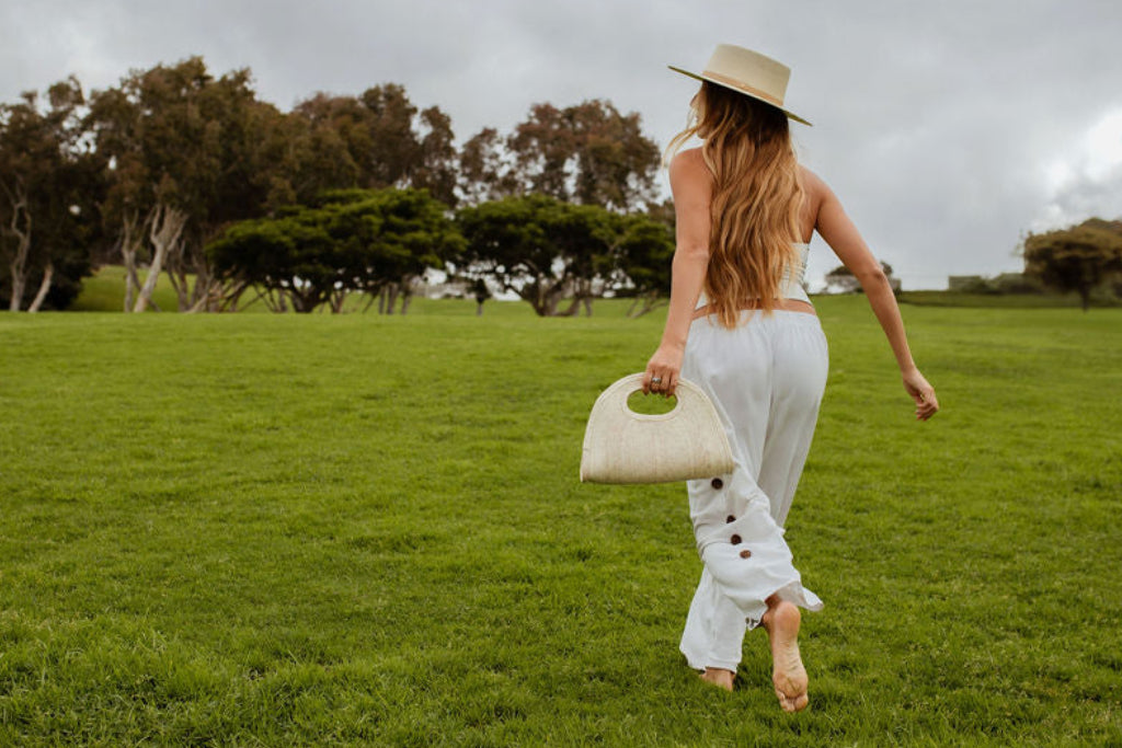Woman in a white outfit and hat walking on a grassy field with a stormy sky.