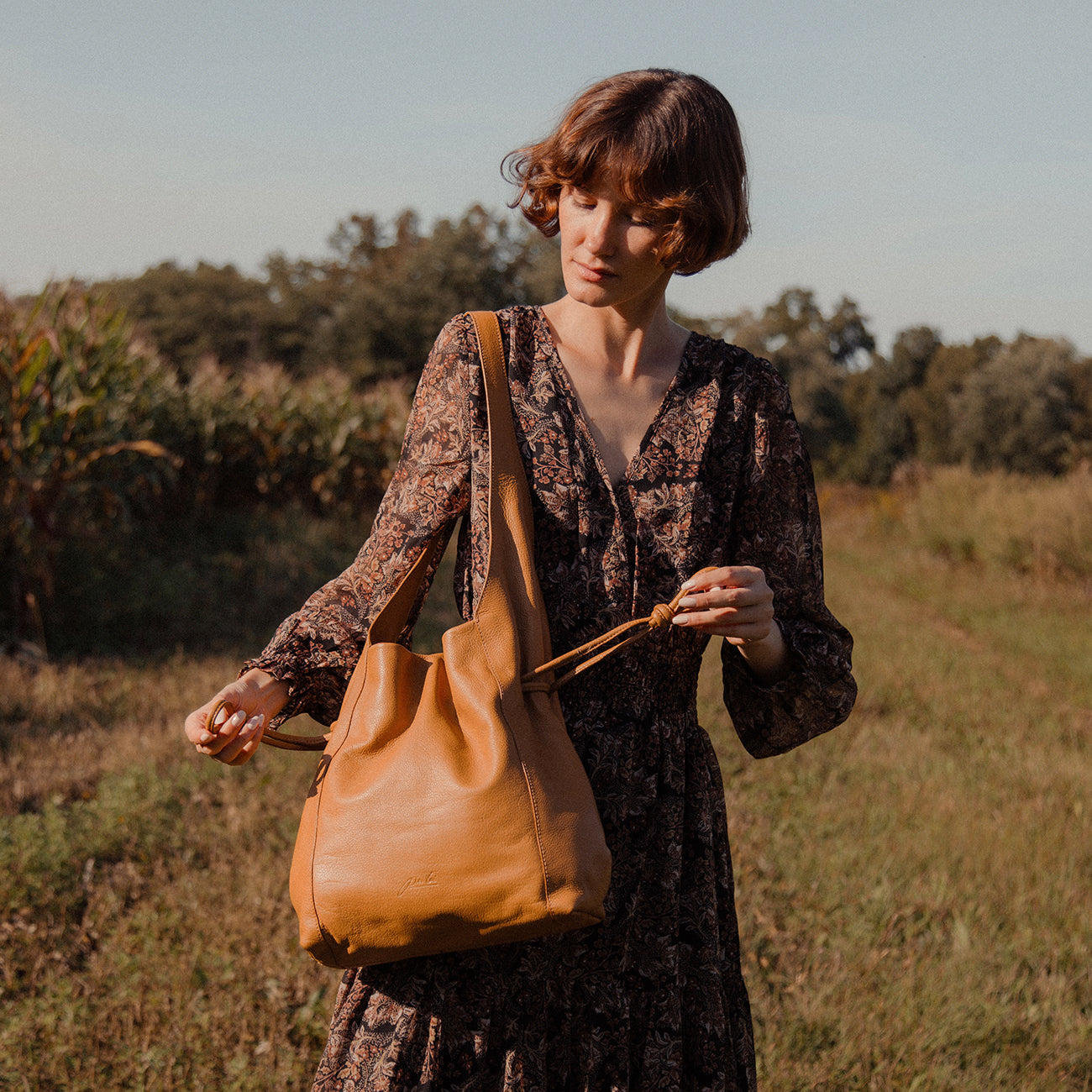 A woman in an dark dress holding a brown leather shoulder drawstring handbag