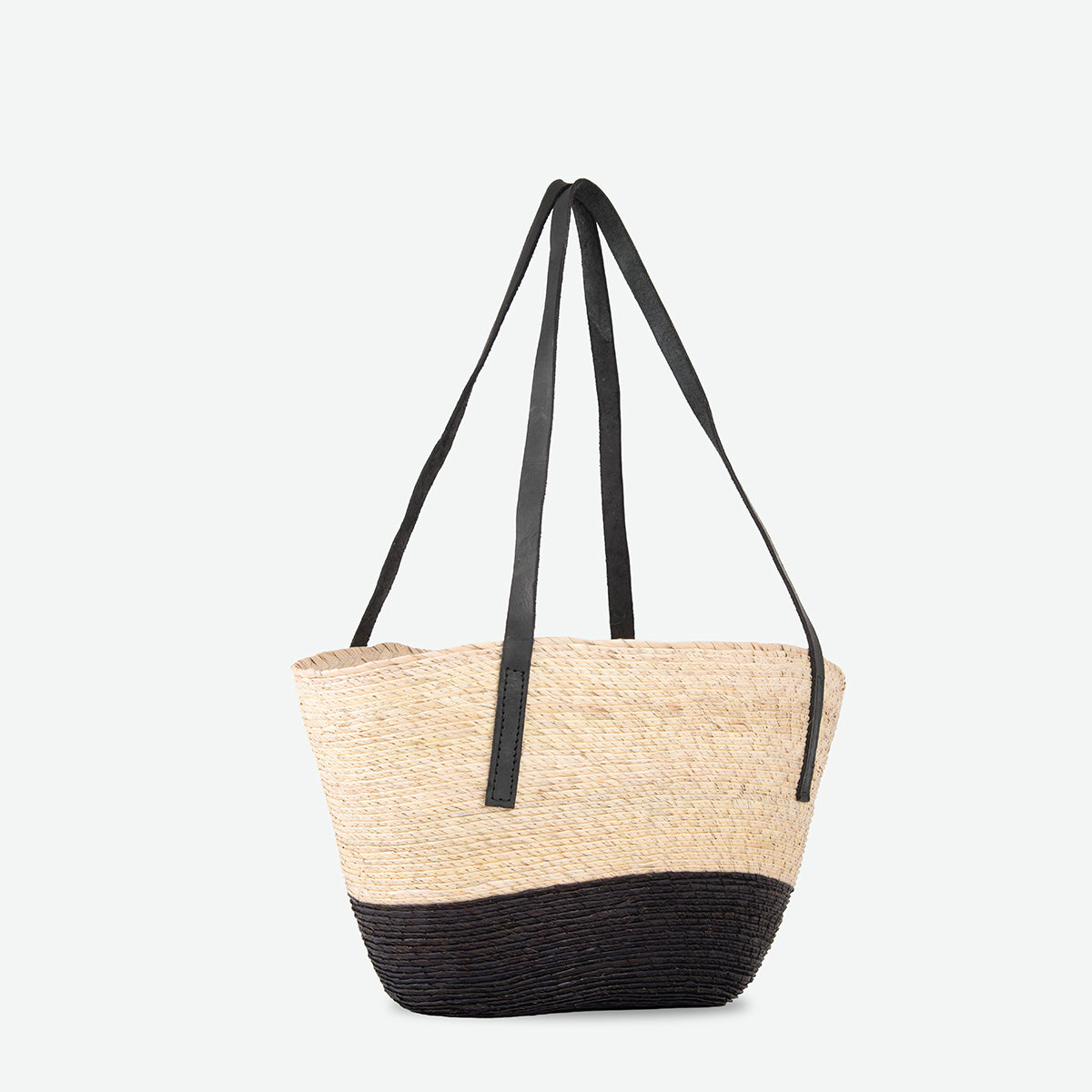 A woven straw tote bag with a black bottom half and black shoulder straps, shown against a plain light gray background.