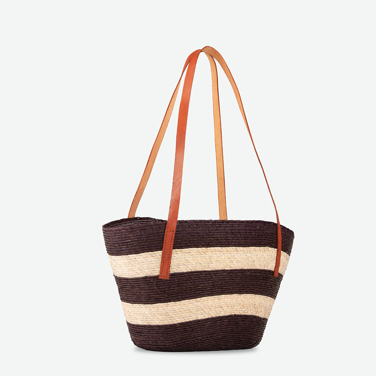 A woven straw tote bag with horizontal dark brown and beige stripes, featuring two long tan leather shoulder straps, shown against a plain light gray background.
