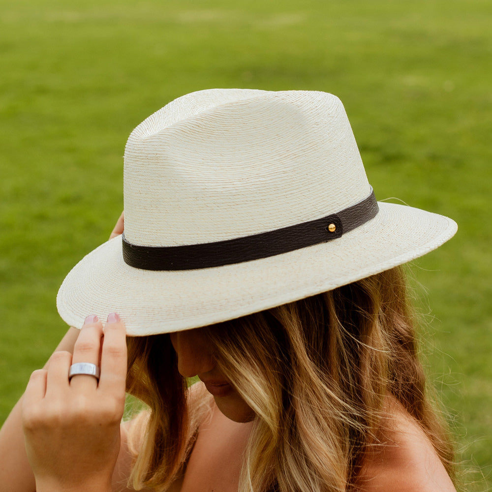 Person wearing a white hat with a black band against a green grass background