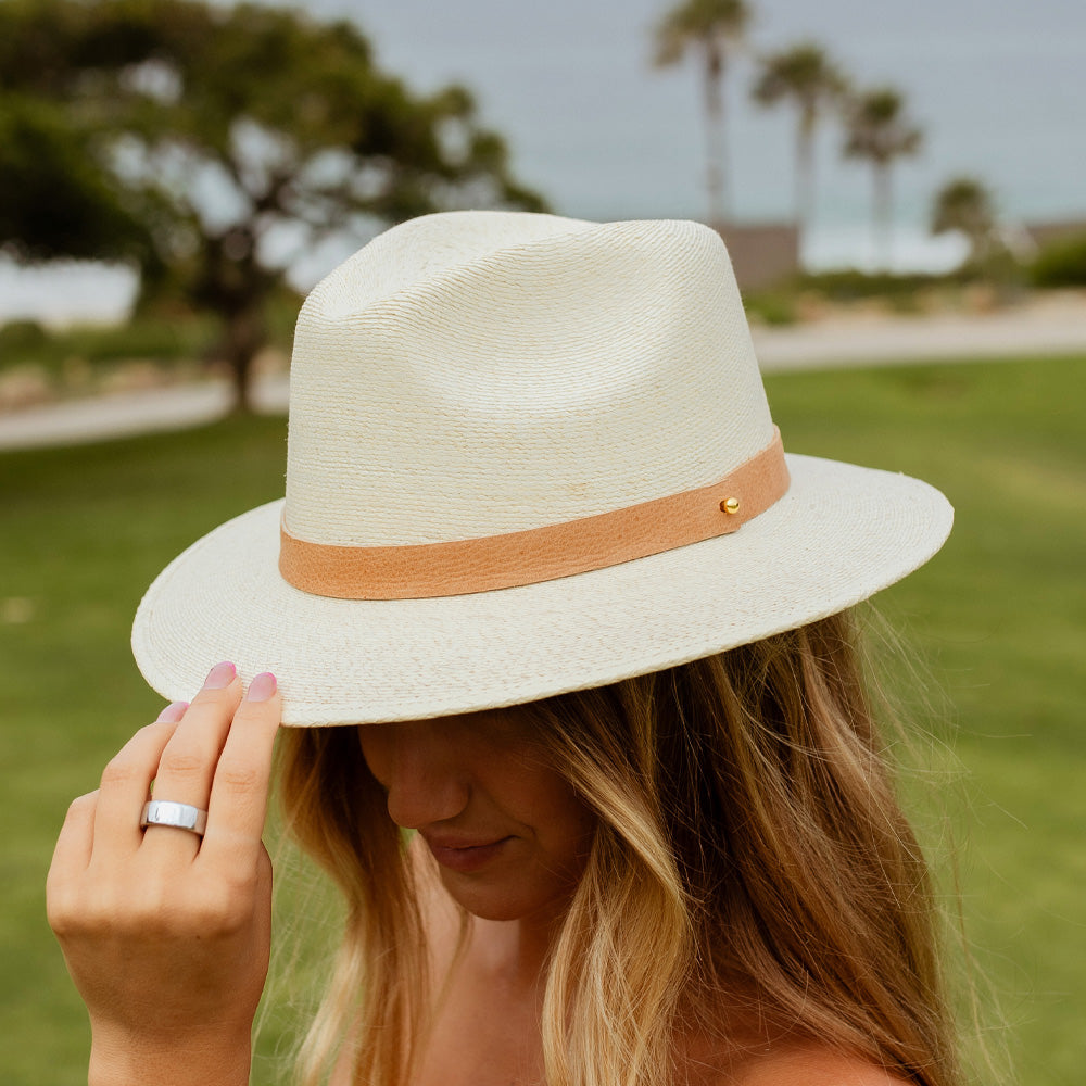 Woman wearing a white straw hat with a brown band outdoors