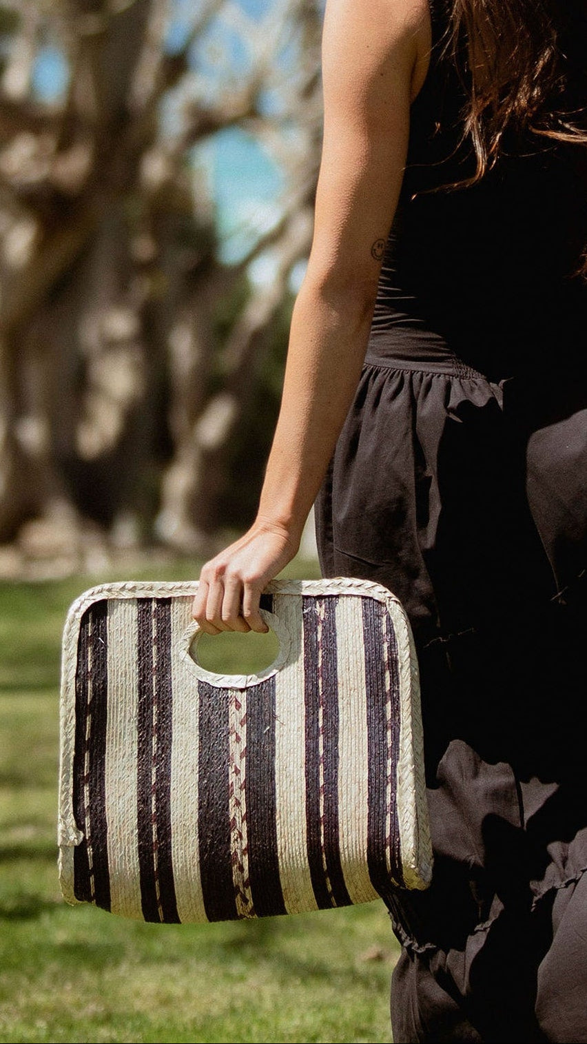 Woman in a black dress holding a striped handbag in a park setting