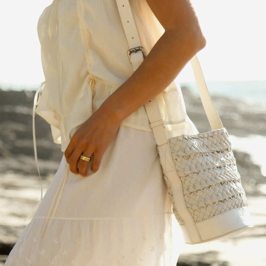 Person wearing a light-colored dress holding a woven leather crossbody handbag